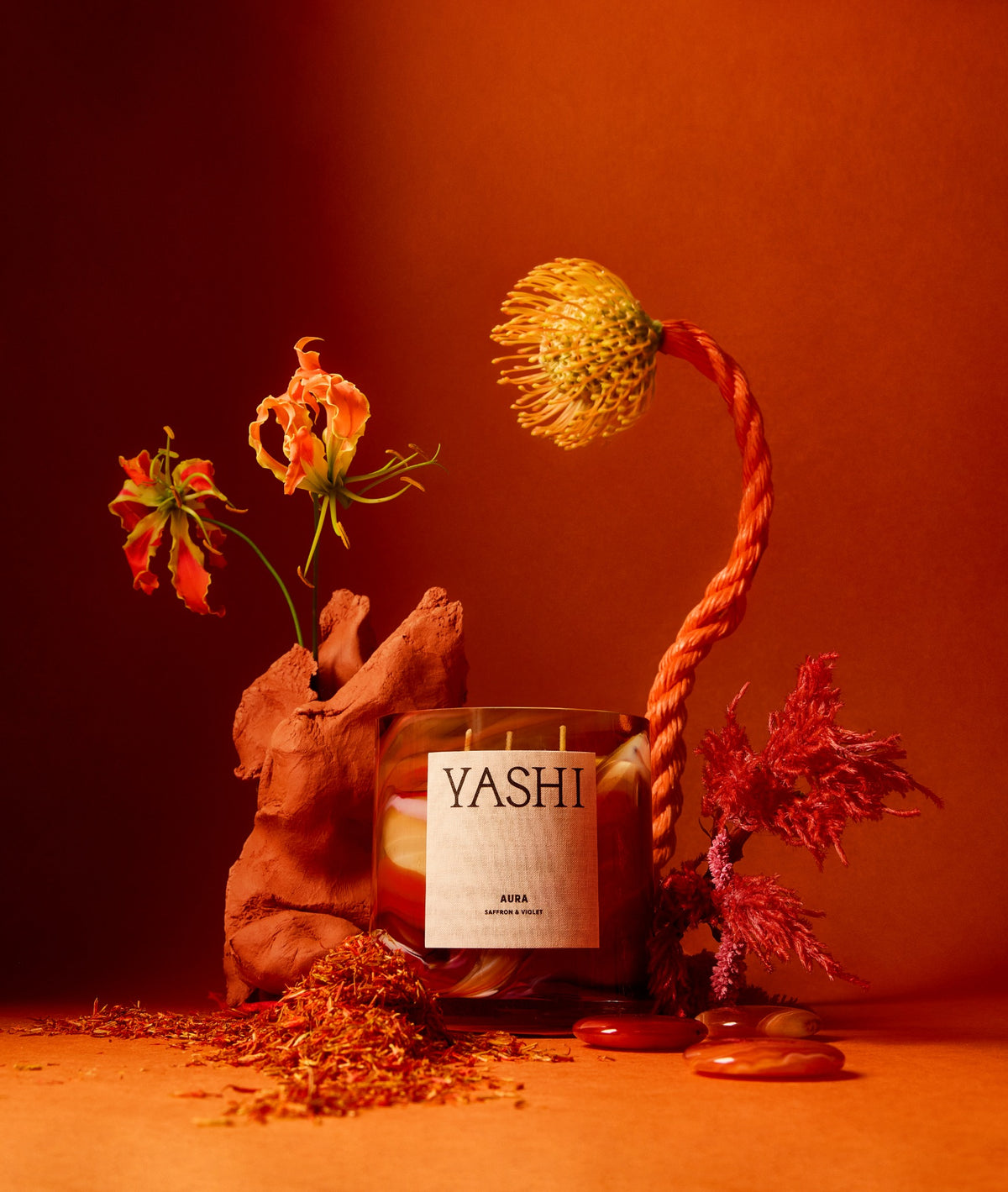 The Yashi Aura candle in a floral setting with deep red tones